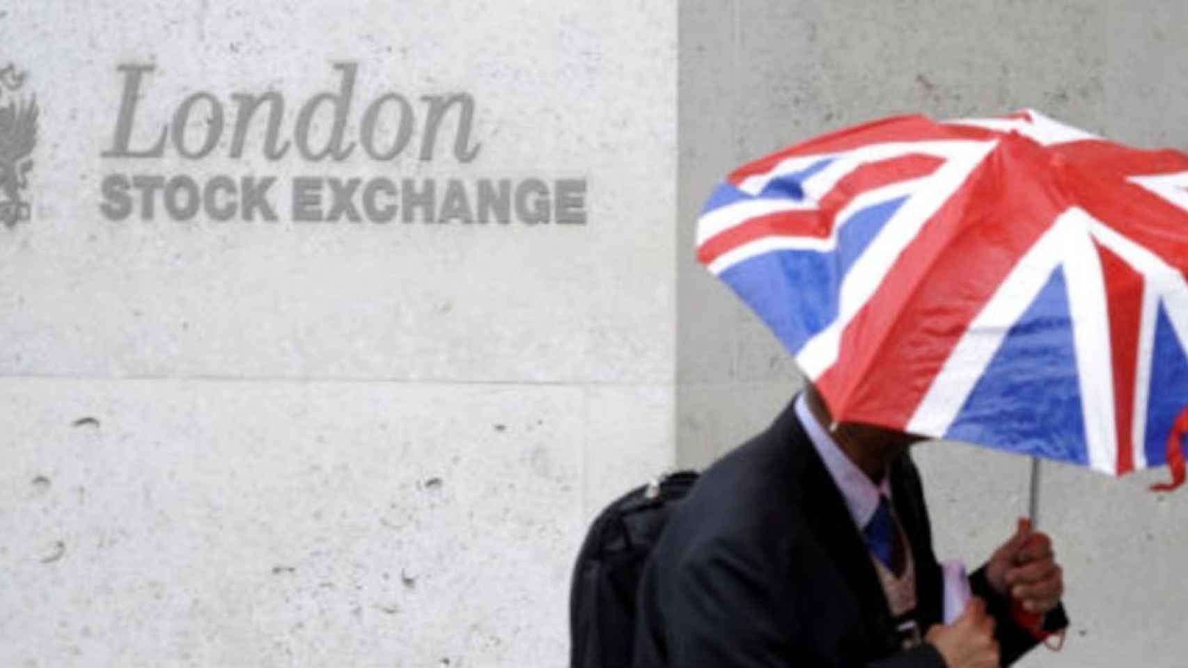 Un bróker pasa por la Bolsa de Londres con un paraguas de la bandera británica.