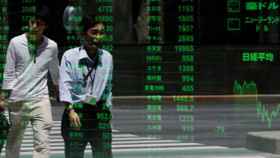 Dos ciudadanos pasan ante una pantalla de cotizaciones de la Bolsa de Tokio.