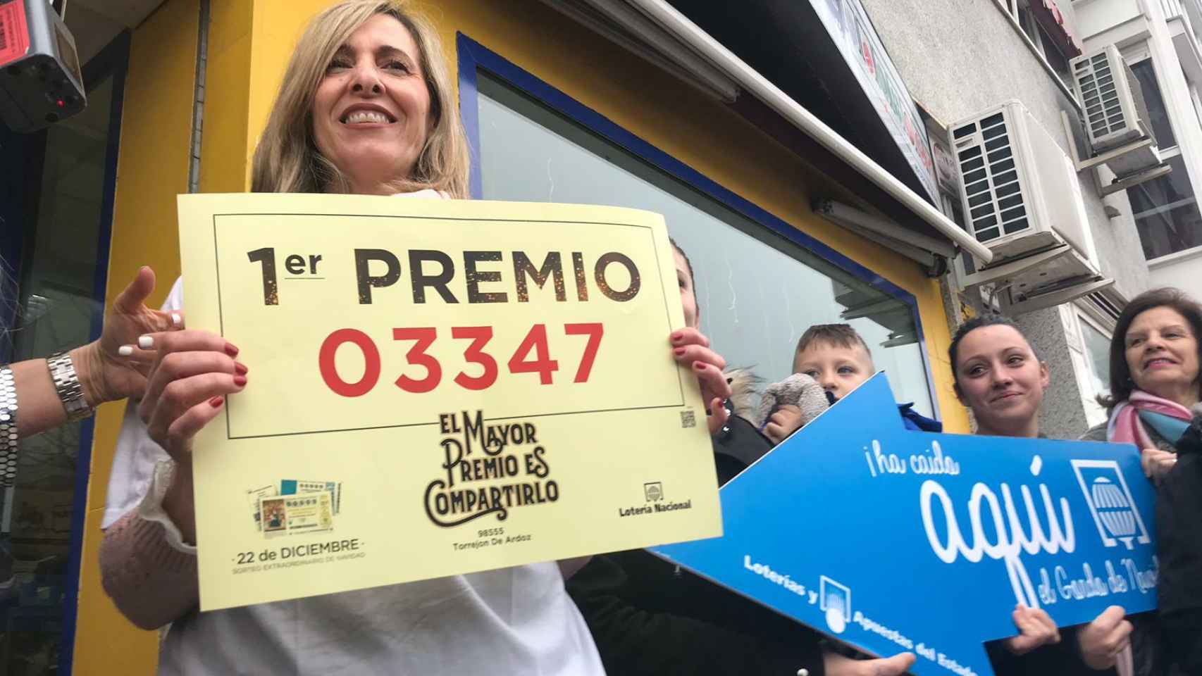 Ana Belén mostrando el número ganador frente a su administración de lotería