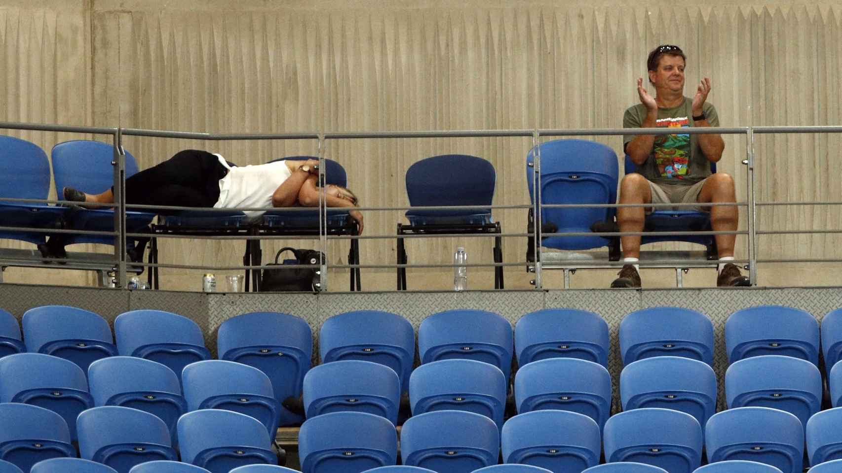 Un aficionado sigue el partido entre Muguruza y Konta mientras otra duerme sobre los asientos.
