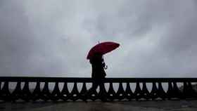 Una mujer camina bajo la lluvia por el paseo marítimo de A Coruña.