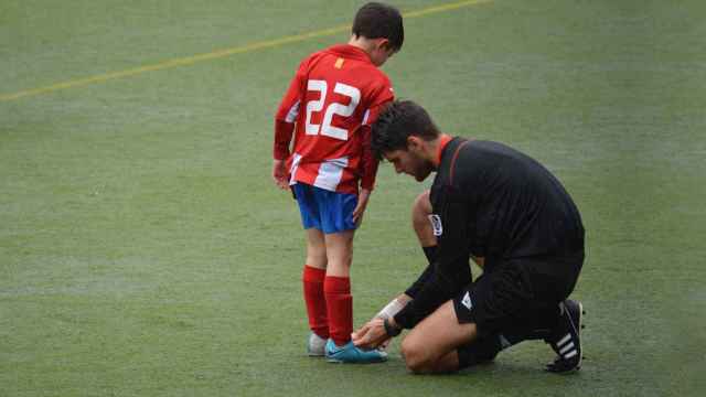 Un árbitro ata los cordones a un niño durante un partido. Foto: Unsplash (Adriá Crehuet Cano)