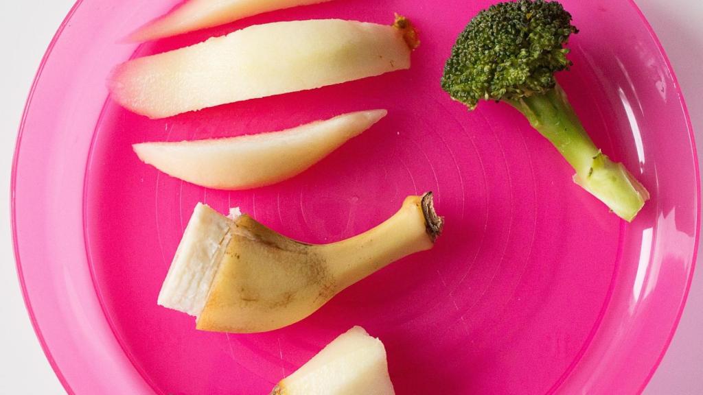 Un plato con unos trozos de manzana, brócoli y un plátano.