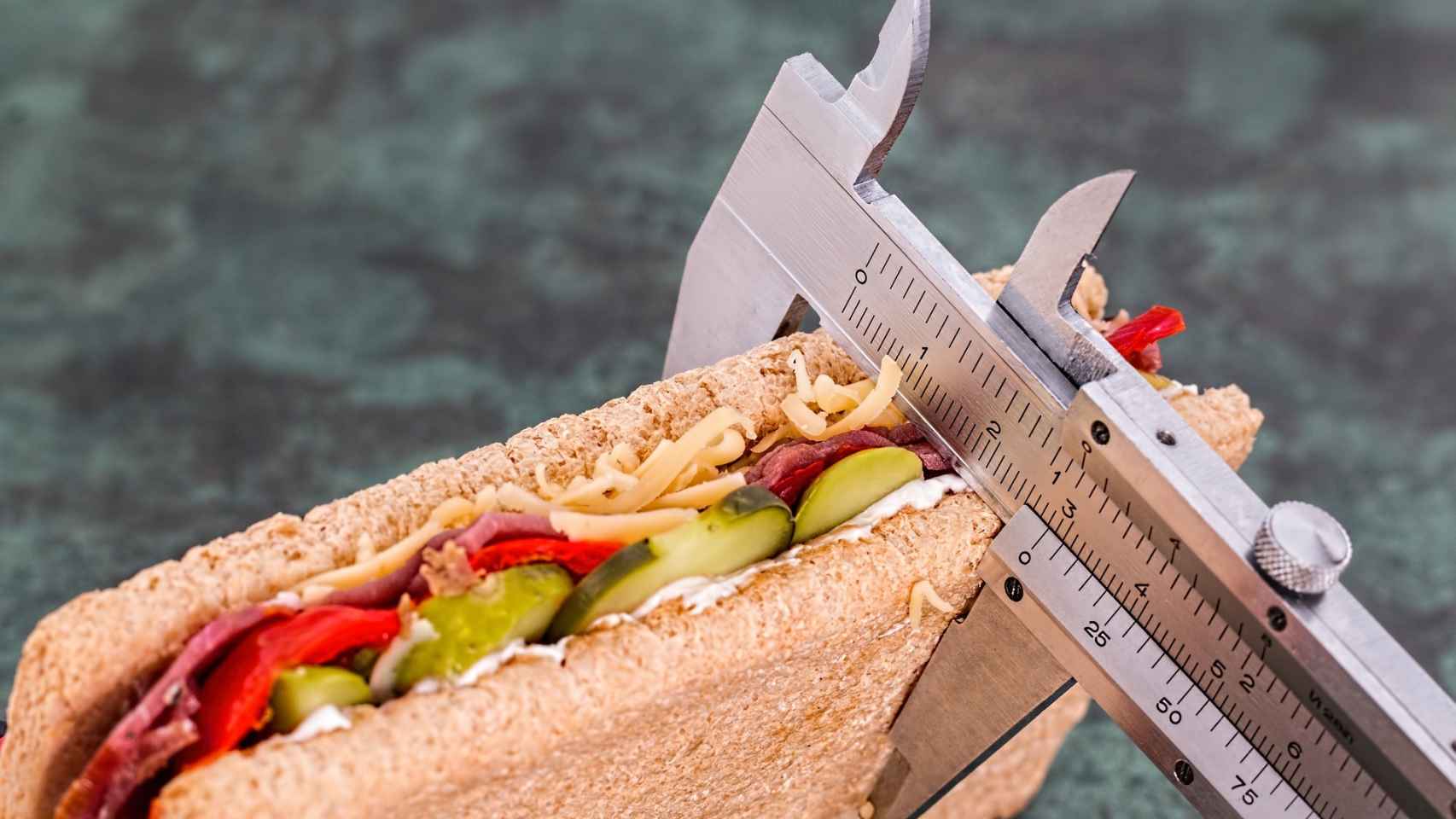 Una persona mide un sandwich vegetal con un calibre.