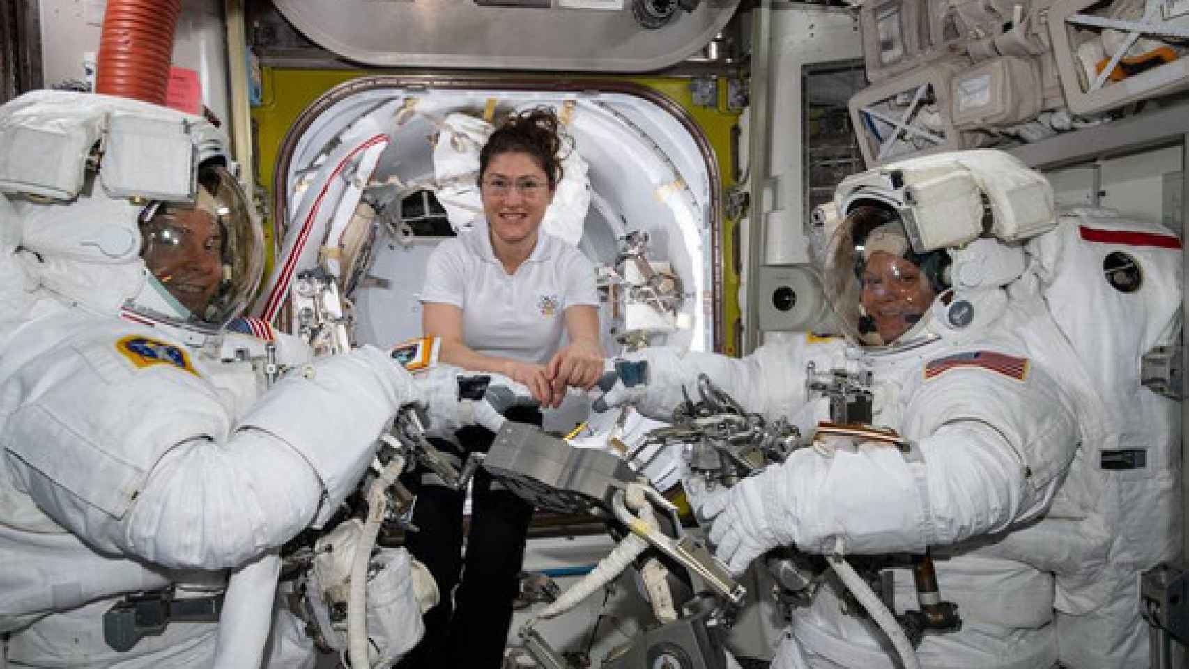La astronauta de la NASA Christina Koch (centro) asiste a sus compañeros astronautas Nick Hague (izquierda) y Anne McClain (derechea) para ajustar sus trajes espaciales poco antes de comenzar su primer paseo espacial el pasado 22 de marzo. /