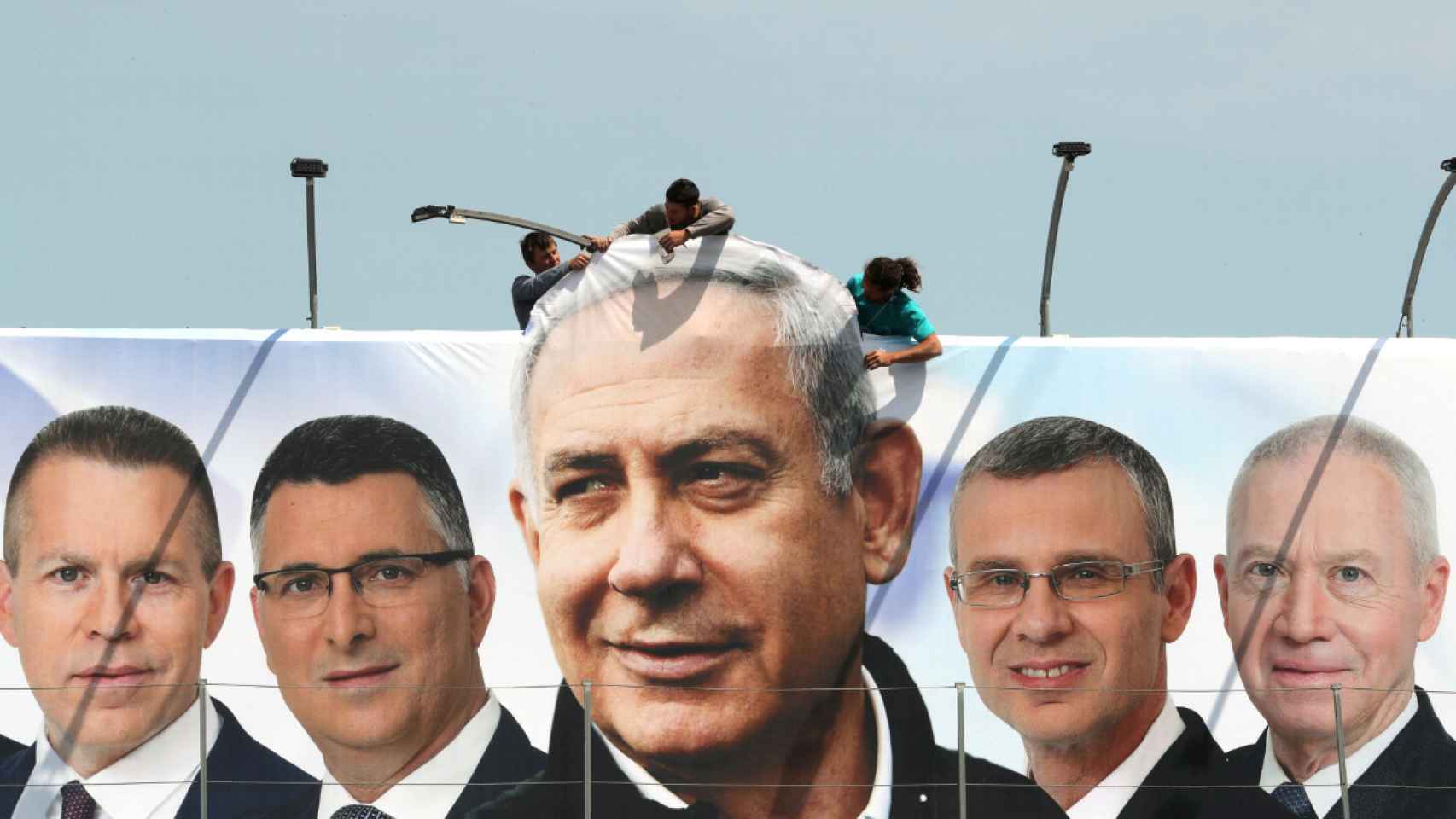 Trabajadores colgando una pancarta de campaña electoral del Likud con Netanyahu en el centro.