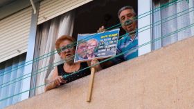 Dos madrileños muestras desde su ventana el cartel electoral de Más Madrid.