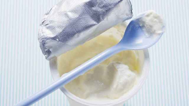 Un yogur abierto con la cuchara apoyada en los bordes del envase.