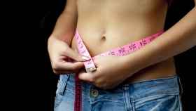 Una joven mide el contorno de su cintura con una cinta métrica.