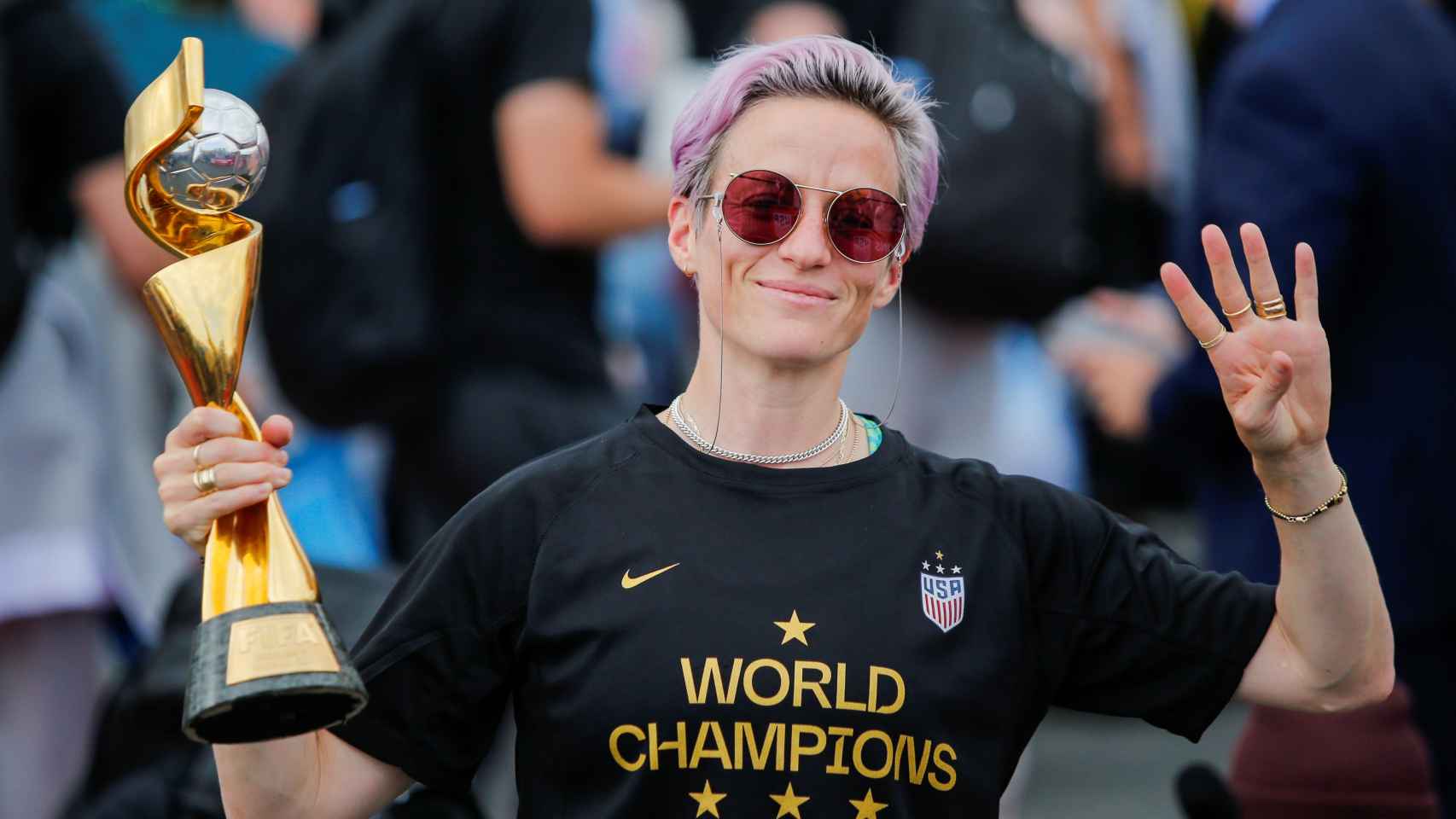 Megan Rapinoe gestures the number 4 with her fingers as she holds the Trophy for the FIFA Women's World Cup while the U.S. team arrives at the Newark International Airport, in Newark