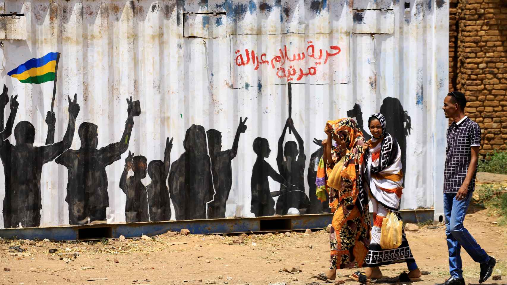 Sudaneses caminan por Jartum y pasan por un mural que reza: Libertad, paz, justicia.