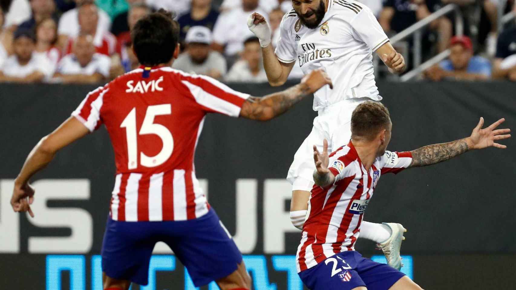 Karim Benzema remata un balón con la cabeza frente a dos jugadores del Real Madrid