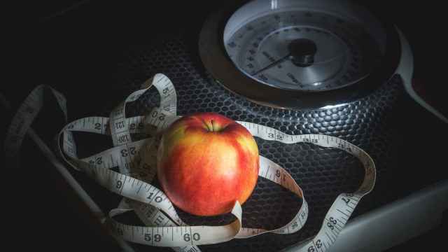 Una cinta métrica y una manzana sobre una báscula.