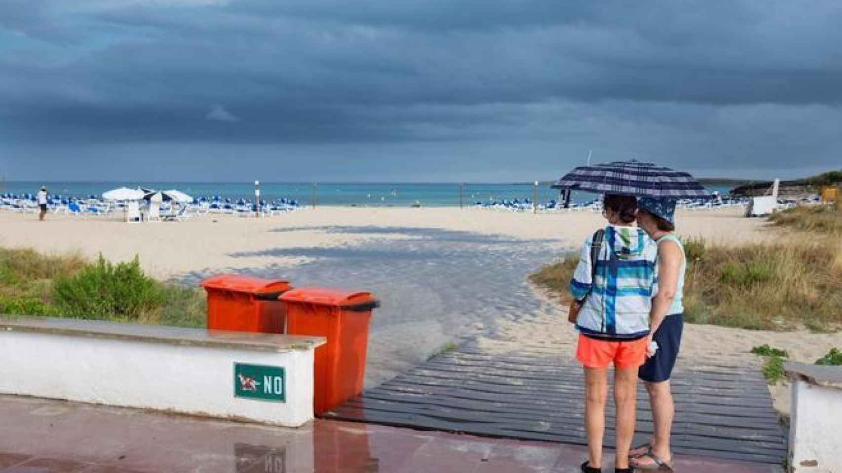 Dos mujeres se resguardan de la lluvia en una playa de Menorca / David Arquimbau Sintes. EFE