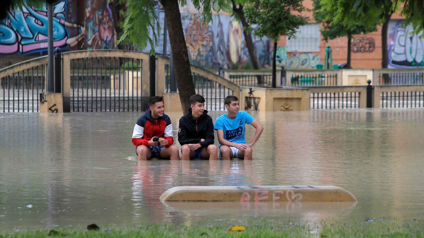 Tres muchachos sentados en un parque pese a la inundación en Orihuela.
