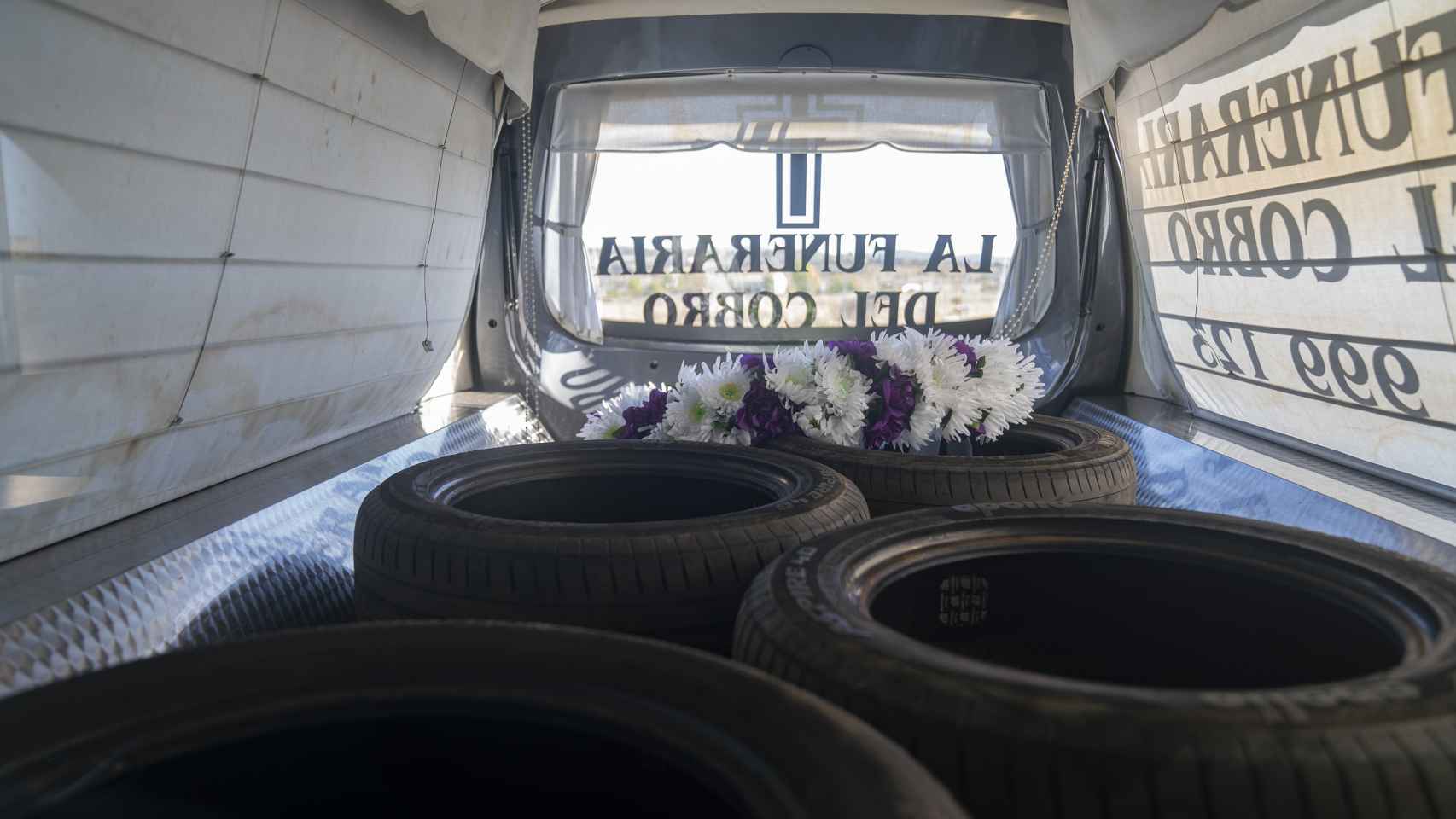 En el interior del coche fúnebre hay una corona de flores y varios recambios de ruedas.