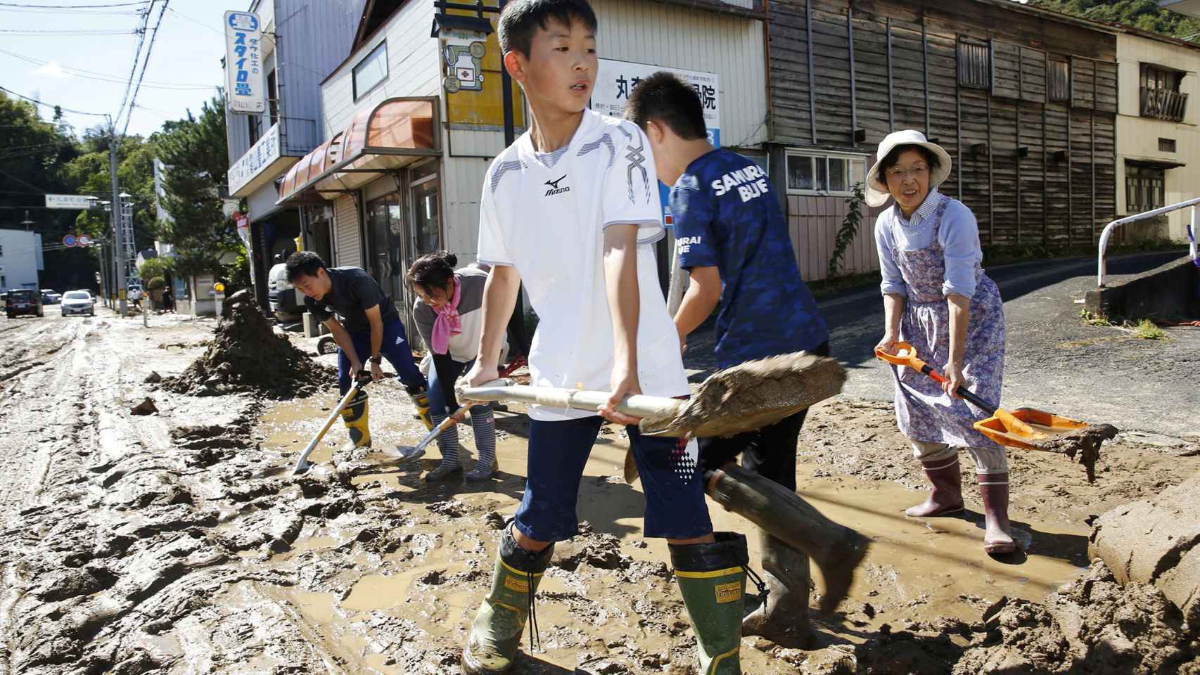 Niños y adultos ayudan a retirar el barro de las calles tras el tifón.