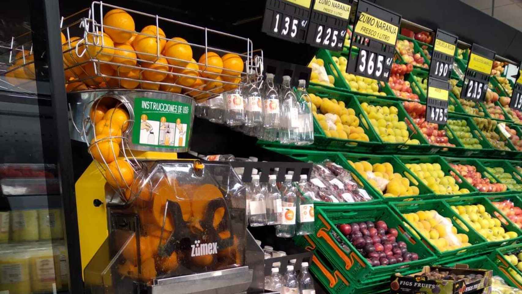 Máquina de zumo y naranjas en la sección de fruta del supermercado.