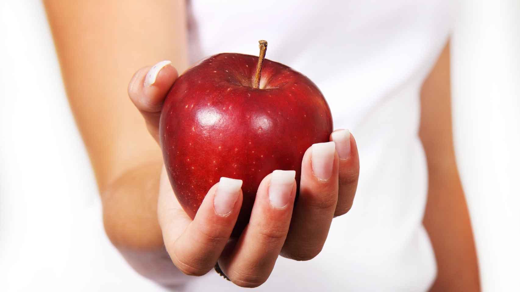 Una mujer sostiene una manzana roja con la mano.