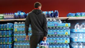 Una hombre escoge una marca de agua embotellada en un supermercado.