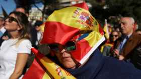 Simpatizante de Vox se protege del sol con una bandera de España durante un acto en Colón, Madrid.