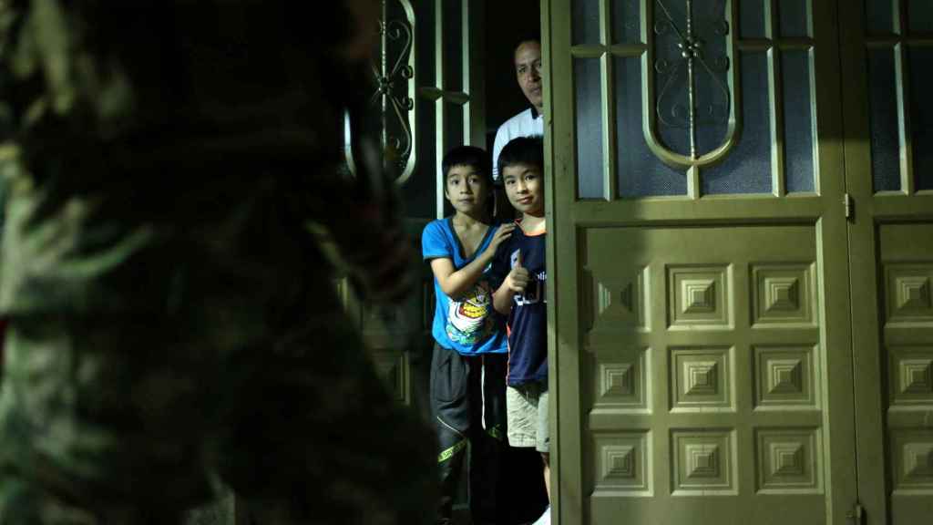Unos niños observan a los militares desde el umbral de una casa durante el toque de queda.