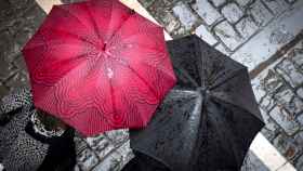 Dos personas pasean por Pamplona bajo sus paraguas.