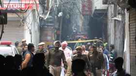 Tres policías caminan entre los escombros de la fábrica que se incendió este domingo en la India.
