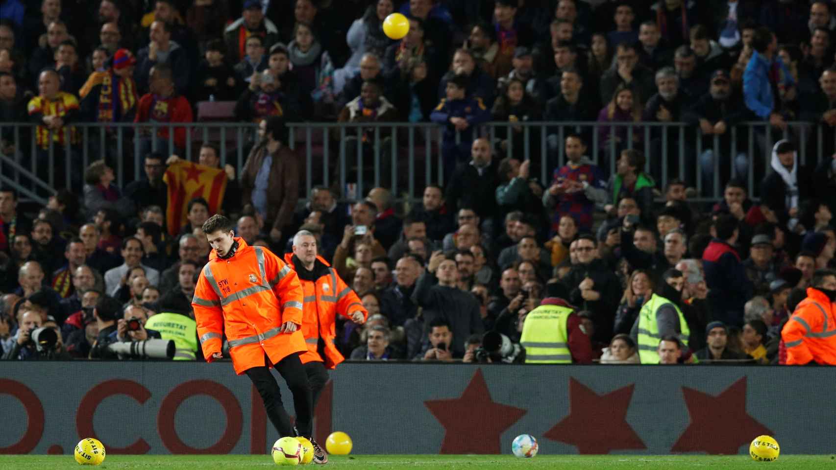 Efectivos de seguridad del Camp Nou intentan sacar del terreno de juego las pelotas amarillas lanzadas desde las gradas
