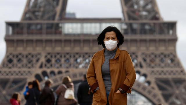 Una mujer camina con mascarilla junto a la Torre Eiffel, en París.