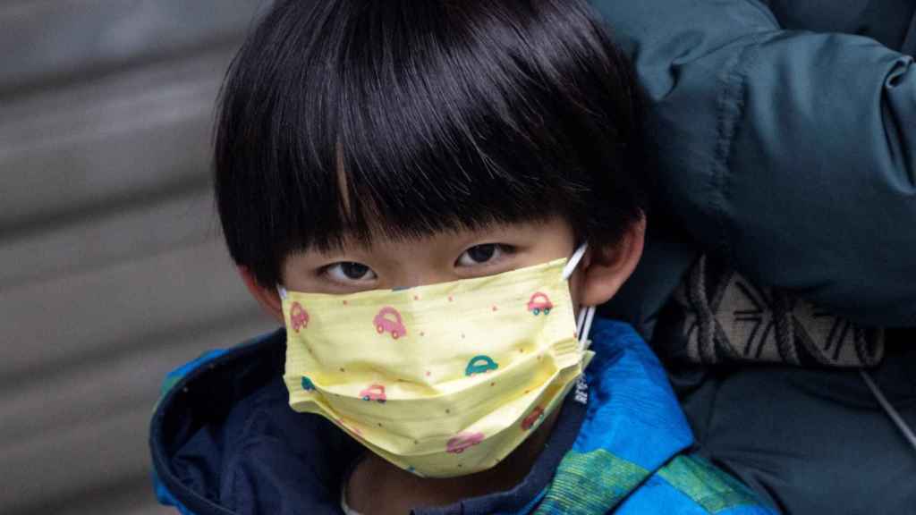 Un niño hace cola en la farmacia para comprarse una mascarilla en China.