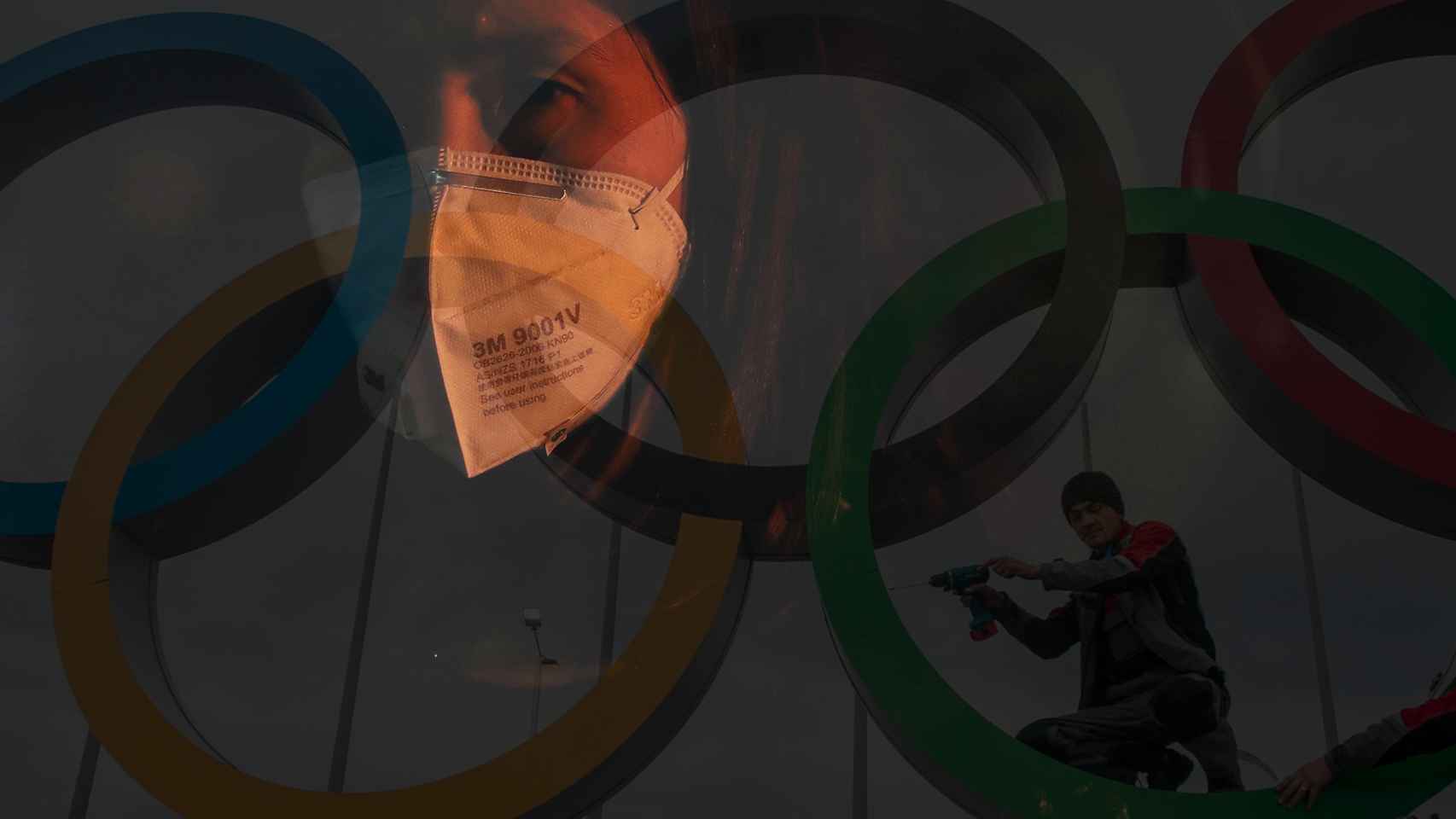 Los aros olímpicos junto a una mujer que porta una máscara por el temor al contagio del coronavirus