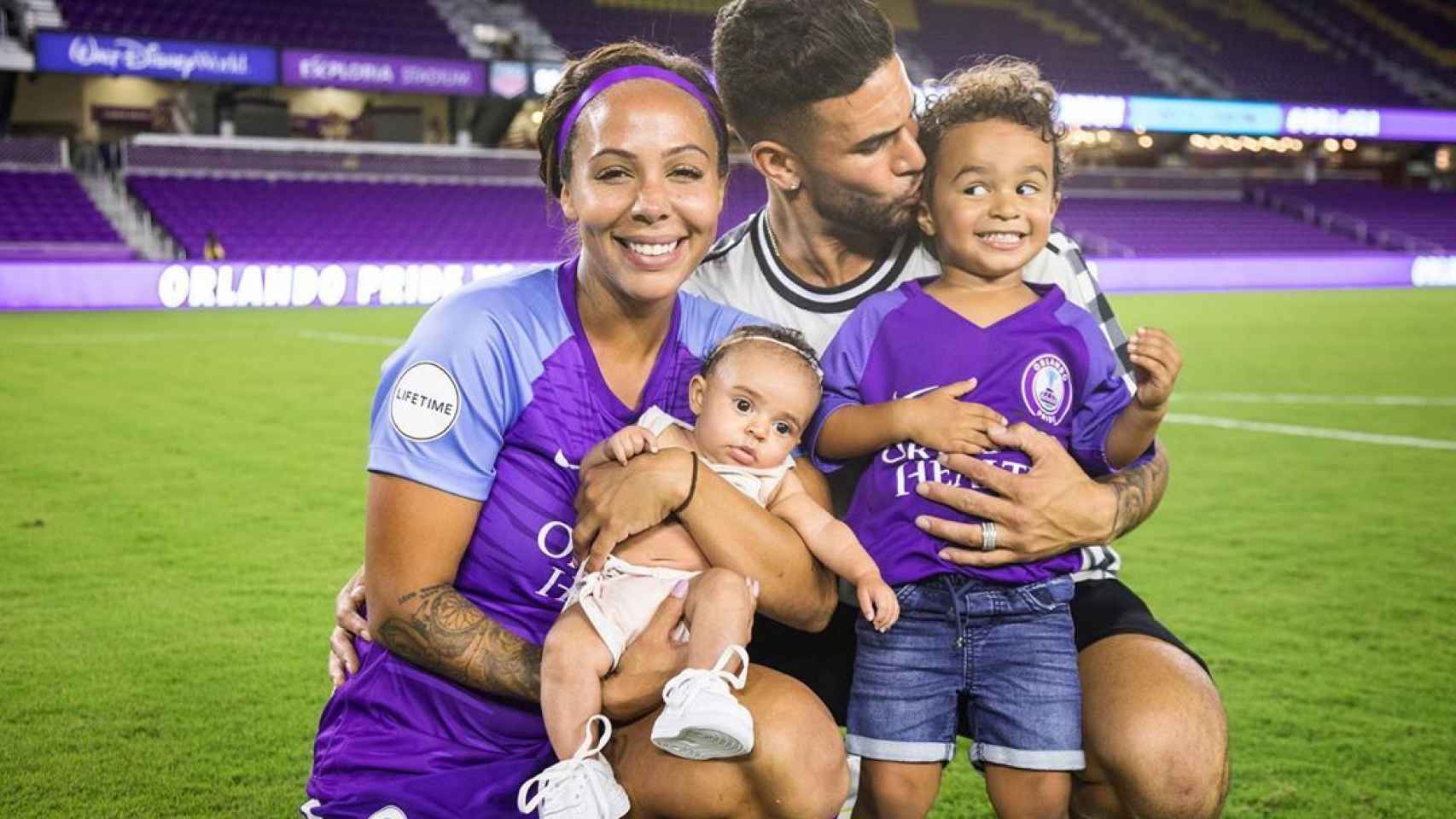 Sydney Lerroux junto a su pareja y sus hijos sobre el césped de un estadio