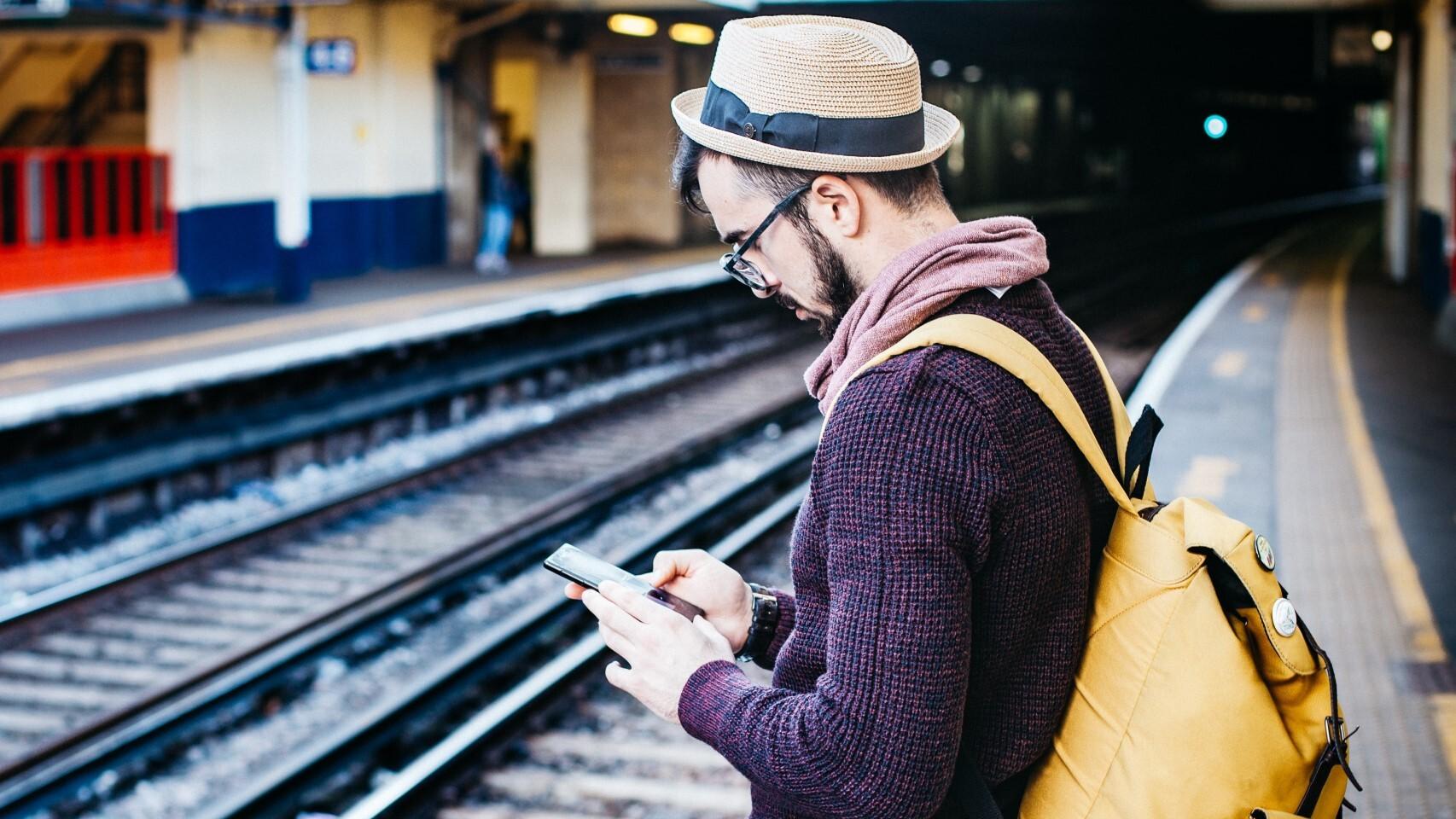 Hombre utilizando su smartphone ante las vías del tren.
