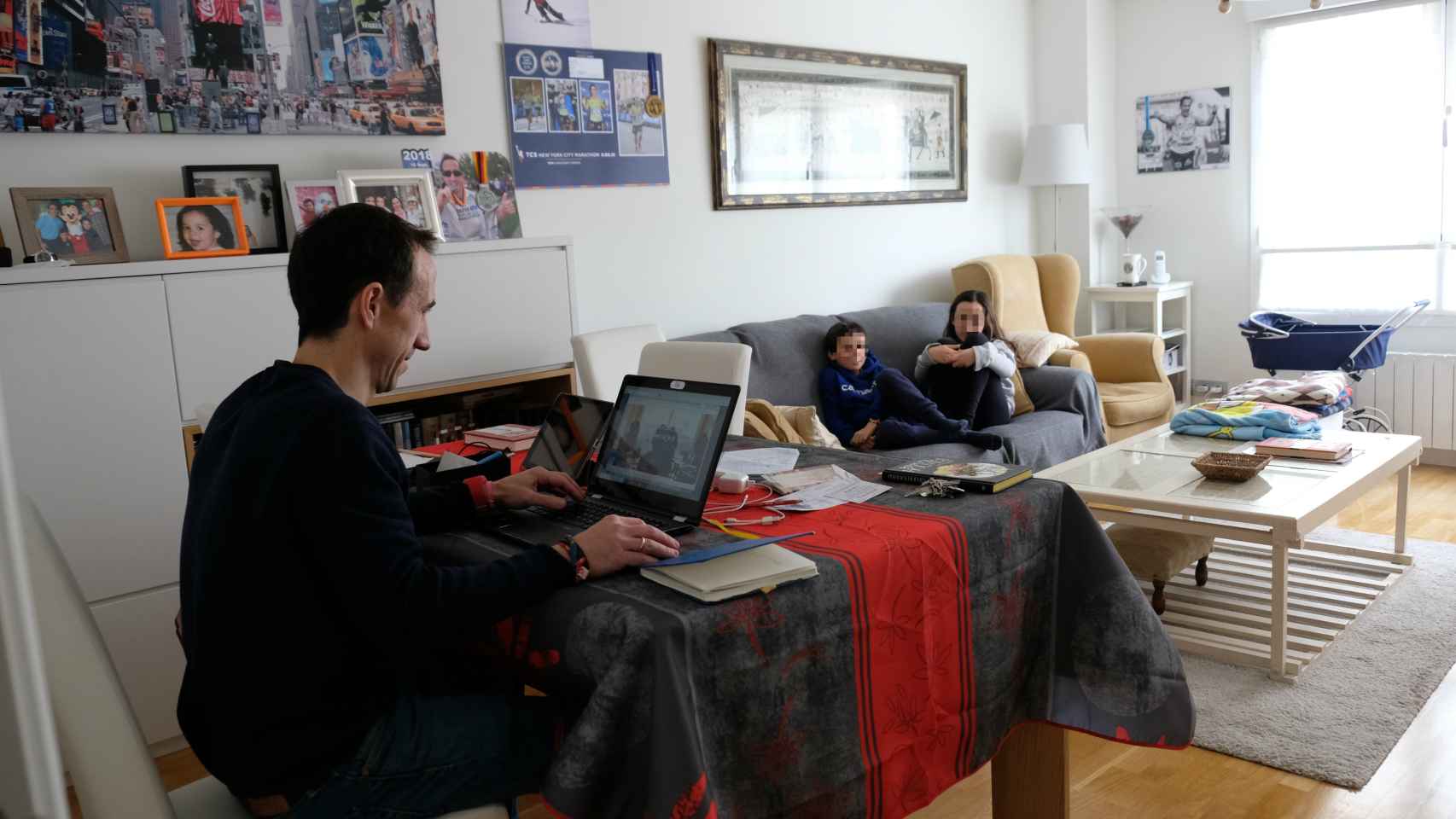 Joaquín, en la mesa, con el ordenador encendido; sus hijos, en el sofá.