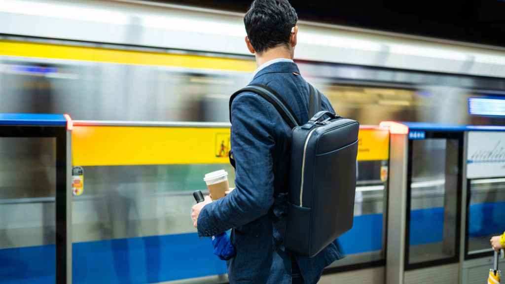 Un trabajador de un distrito financiero espera el tren con mochila.