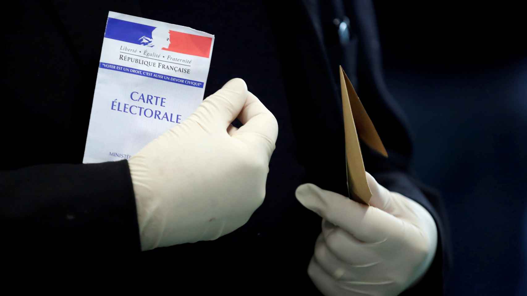 Un hombre con guantes de látex porta su tarjeta electoral antes de votar, en París.