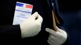 Un hombre con guantes de látex porta su tarjeta electoral antes de votar, en París.