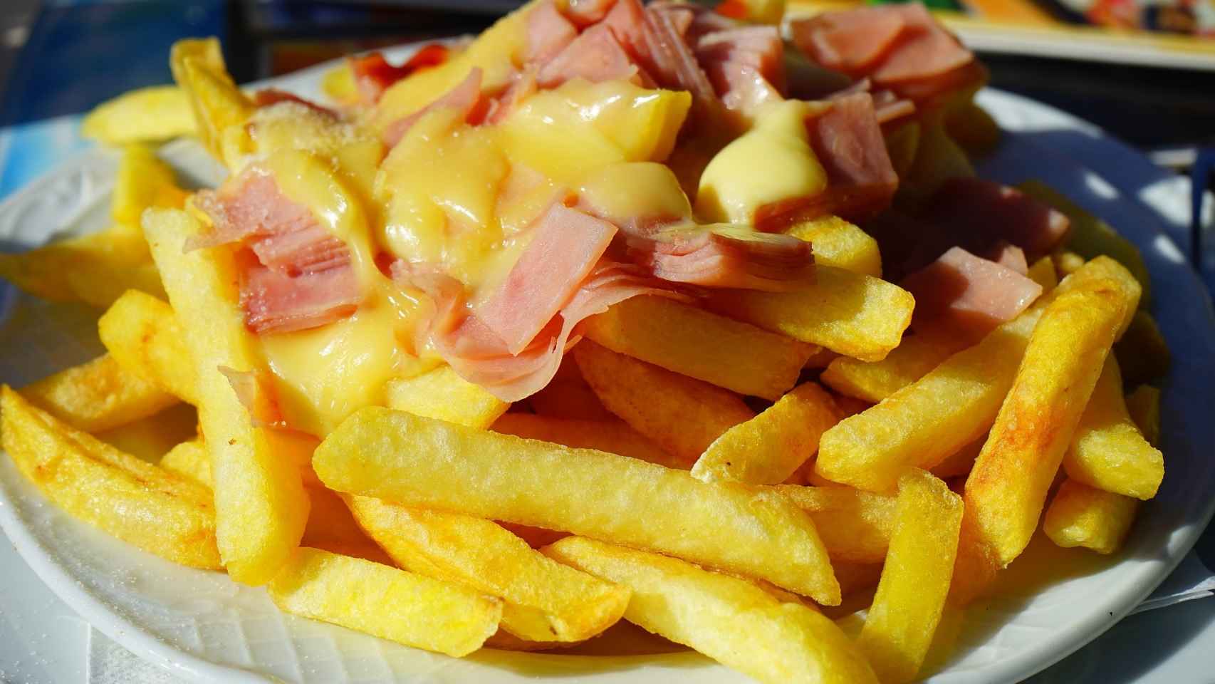 Un plato de patatas fritas con jamón y salsa de queso.