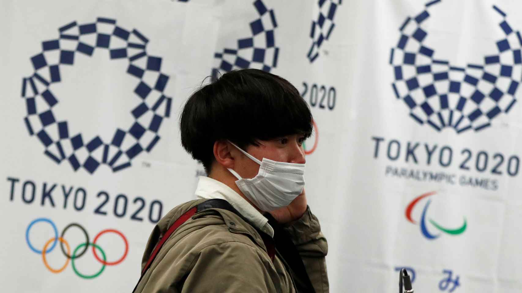 Un joven japonés con mascarilla, delante del logo de Tokio 2020