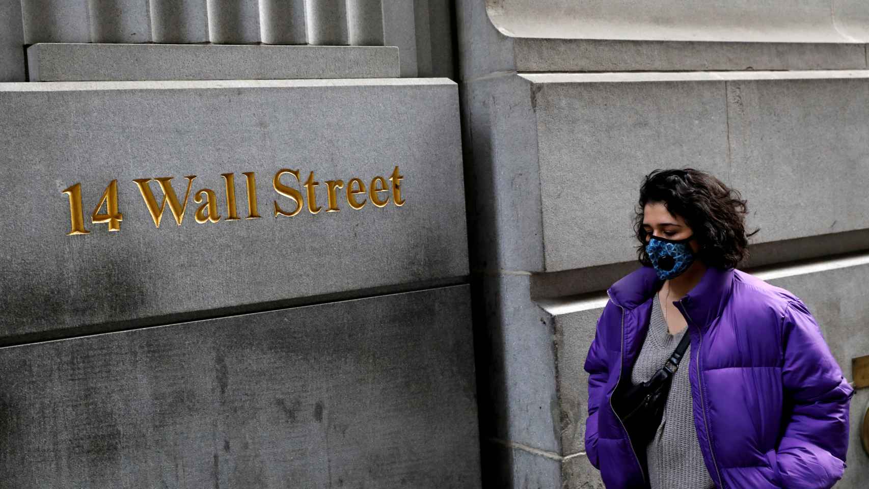 Una mujer lleva una mascarilla en su paseo por Wall Street.