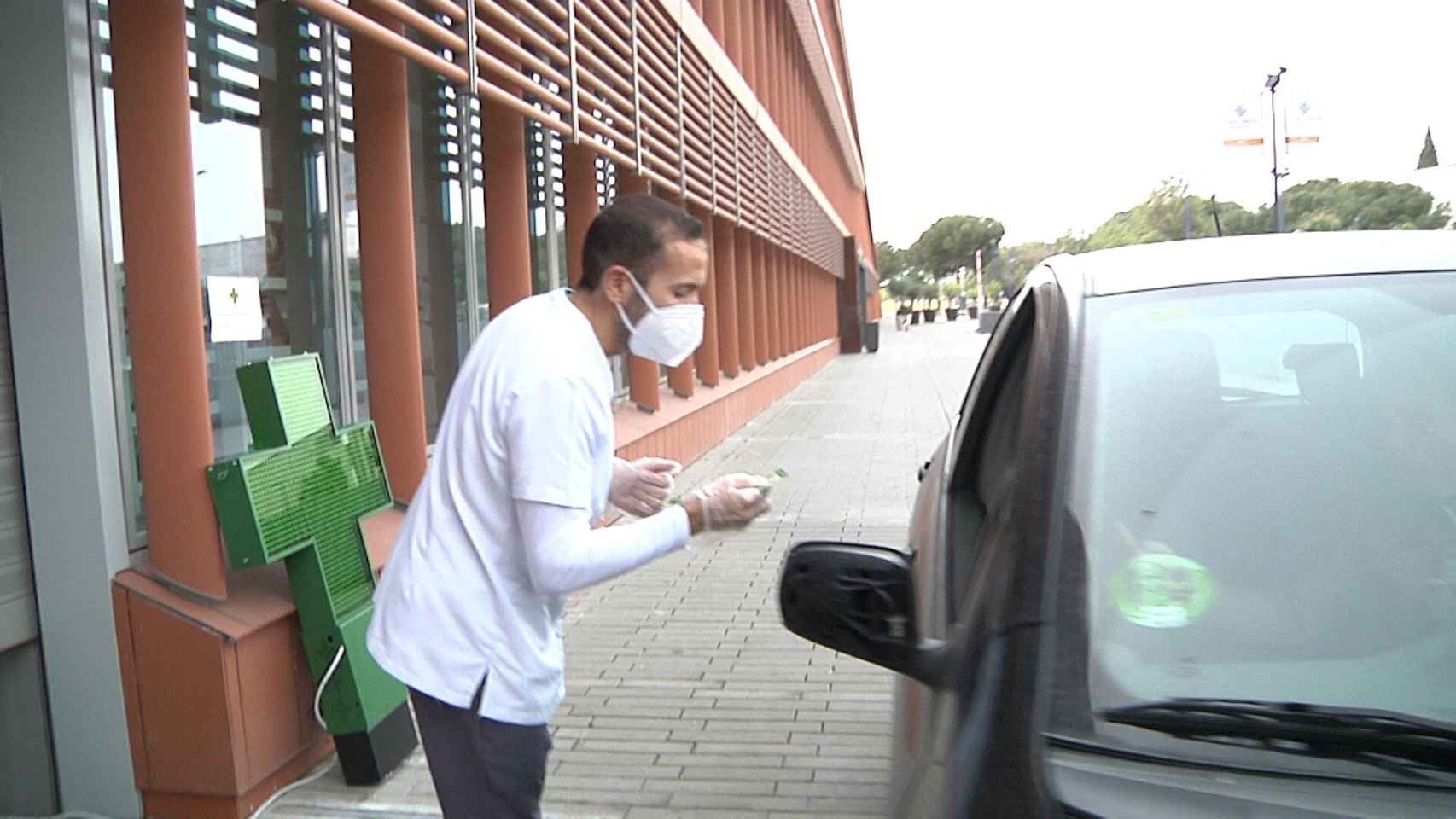 Una farmacia en Torre (Sevilla), permite recoger medicamentos desde los coches para evitar el contacto. En imagen, el farmacéutico entregando el producto.