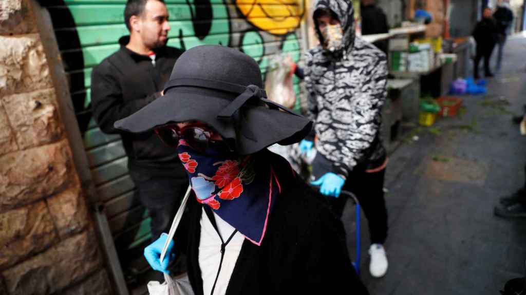 Una mujer ataviada con una mascarilla pasea por una calle de Jerusalén.