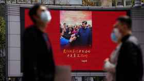 Pedestrians wearing face masks walk past a screen displaying an image of Chinese President Xi Jinping in Shanghai