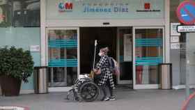 Una mujer con una máscara sanitaria porta una silla de ruedas en los exteriores del Hospital Universitario Fundación Jiménez Díaz de Madrid.