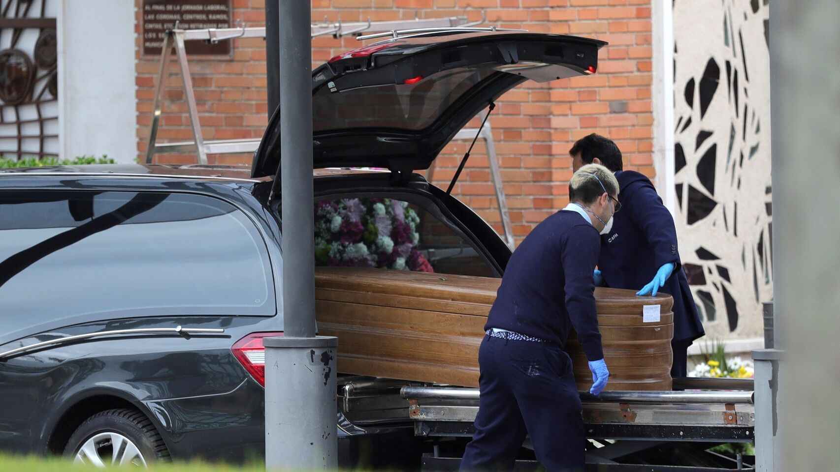 Trabajadores de una funeraria introducen un ataúd en un coche fúnebre.