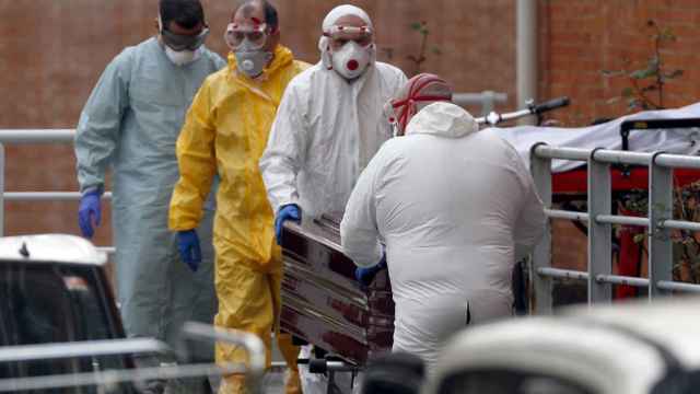 Trabajadores de una funeraria protegidos trasladan de la morgue a un fallecido por coronavirus.