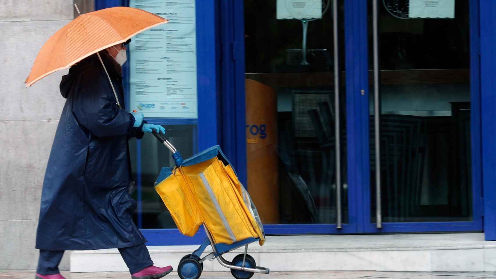 Una cartera, protegida con mascarilla, reparte el correo bajo la lluvia, este martes en Valencia.