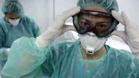 Un sanitario se coloca sus gafas de protección, ataviado con mascarilla y bata quirúrgica.