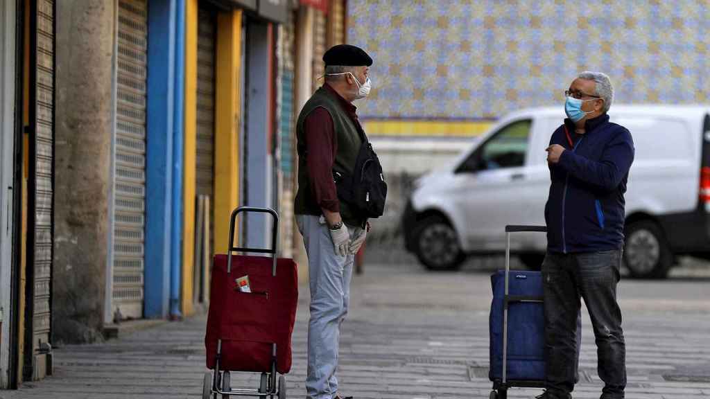 Dos hombres conversan manteniendo las distancias a las puertas del Mercado Central de València. EFE/Manuel Bruque